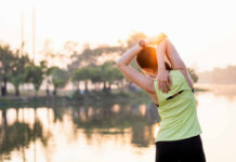 The Workout Formula That Defies Brain Aging A woman stretching her arms by a lake during sunrise
