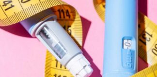 An insulin pen and measuring tape on a pink background