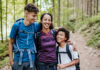 A mother and her two children smiling while hiking on a forest trail