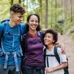 A mother and her two children smiling while hiking on a forest trail
