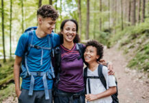 A mother and her two children smiling while hiking on a forest trail