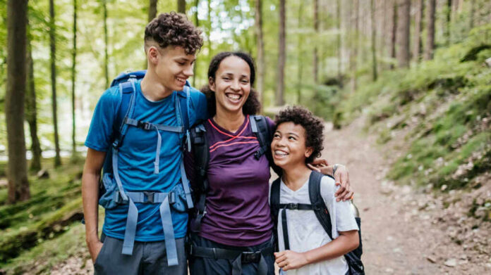 A mother and her two children smiling while hiking on a forest trail