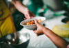 A person handing a bowl of food to another person in a communal setting