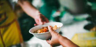 A person handing a bowl of food to another person in a communal setting
