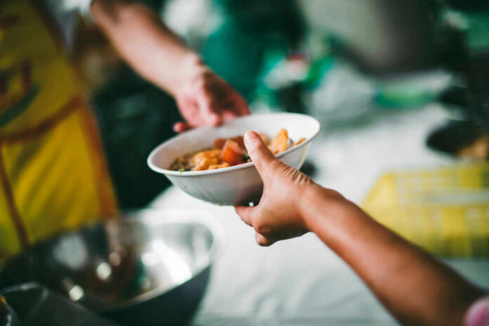 A person handing a bowl of food to another person in a communal setting