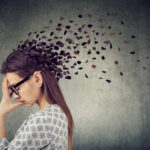 Cord-Cutting: The Secret to Emotional Freedom A woman with glasses holding her head, with fragments dispersing from her head