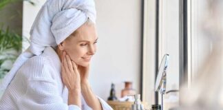 Woman in a bathrobe with a towel on her head, smiling at her reflection in a mirror
