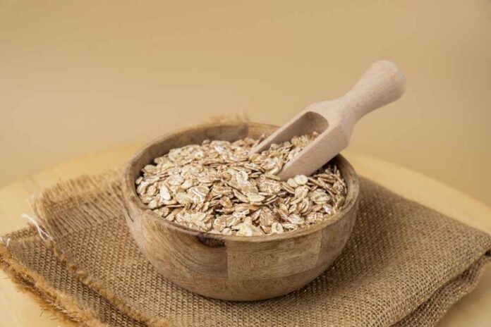 A wooden bowl filled with oats and a wooden scoop