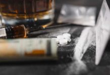 A close-up of a syringe, pills, and a glass of alcohol on a dark surface