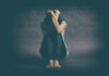 A person sitting on the floor with their arms wrapped around their knees, conveying a sense of distress