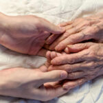 Aging’s Shocking Two-Stage Process A younger persons hand gently holding an elderly persons hand on a quilted surface
