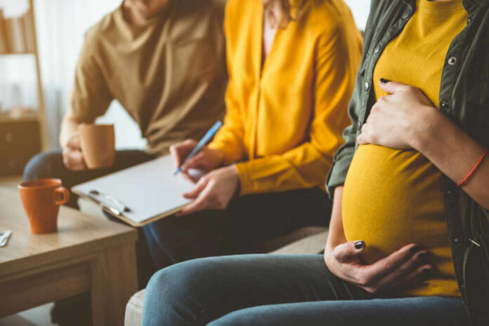 shutterstock_1095110036 Pregnant woman sitting with two people discussing notes in a cozy living room
