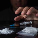 A hand reaching for a syringe next to a pile of white powder