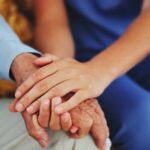 An elderly persons hand being held by a younger persons hand, symbolizing care and support