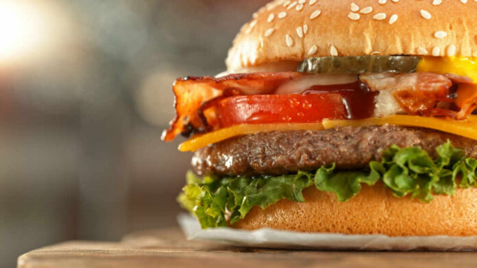 shutterstock_2478584561 Close-up of a juicy hamburger with bacon, lettuce, tomato, and cheese