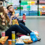 NOVA Revelation: Foods You Thought Were Safe! A young couple sitting on the floor of a grocery store enjoying snacks