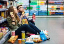 Ultra-Processed Trap — Engineered Cravings? A young couple sitting on the floor of a grocery store enjoying snacks