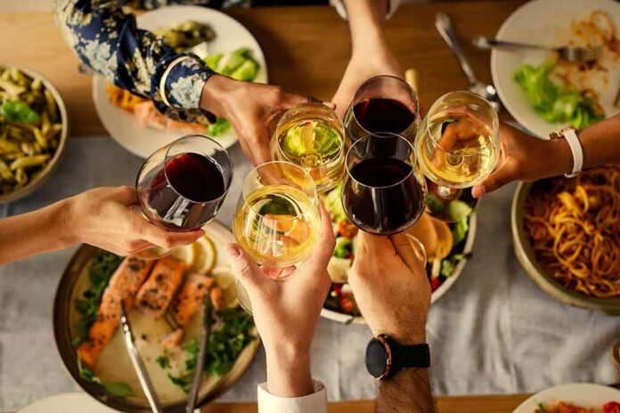 shutterstock_1097487464 Hands clinking wine glasses over a dinner table