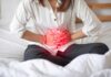Woman holding her abdomen in pain while sitting on a bed
