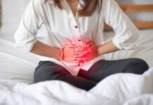 Woman holding her abdomen in pain while sitting on a bed