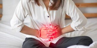 Woman holding her abdomen in pain while sitting on a bed