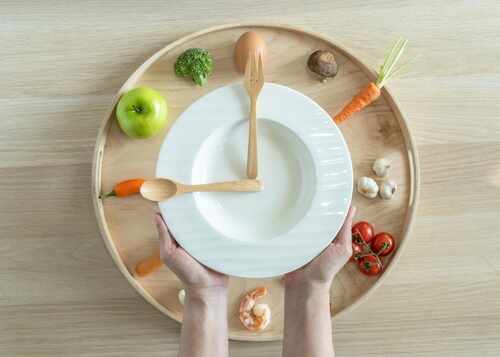 Hands holding a white plate surrounded by fresh vegetables and an egg