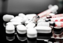 White pills and syringes arranged on a reflective surface