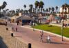 People walking and biking along a beach promenade with palm trees