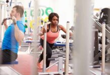 Woman performing sled push in a gym beside a man using a cable machine