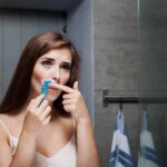 Woman shaving upper lip in bathroom mirror