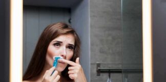 Woman shaving upper lip in bathroom mirror