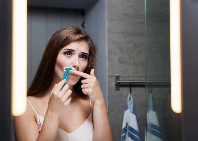 Woman shaving upper lip in bathroom mirror