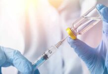 Gloved hands draw liquid from a vial into a syringe