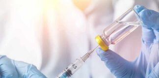 Gloved hands draw liquid from a vial into a syringe