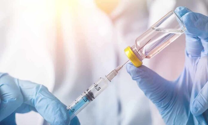 Gloved hands draw liquid from a vial into a syringe