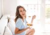 How to Create a Personalized Wellness Plan That Sticks Woman sitting on a couch eating a bowl of fruit salad