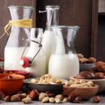 Glass bottles of milk surrounded by assorted nuts in bowls