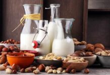 Glass bottles of milk surrounded by assorted nuts in bowls