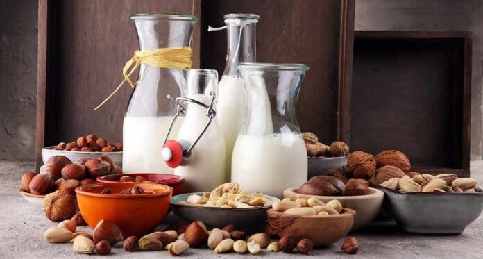 Glass bottles of milk surrounded by assorted nuts in bowls