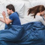 Couple sleeping back to back in bed under blue blanket