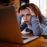 Woman holding head while looking at laptop