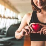Woman in sportswear holding a red heart-shaped object at the gym