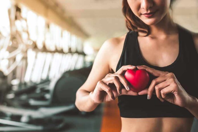 Woman in sportswear holding a red heart-shaped object at the gym