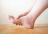 Hand holding the arch of a bare foot on a wooden floor