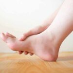 Hand holding the arch of a bare foot on a wooden floor