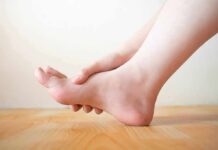 Hand holding the arch of a bare foot on a wooden floor