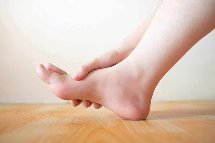 Hand holding the arch of a bare foot on a wooden floor