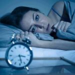 Woman lying awake in bed beside an alarm clock