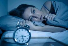 Woman lying awake in bed beside an alarm clock