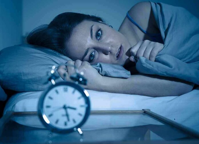 shutterstock_1452406124 Woman lying awake in bed beside an alarm clock